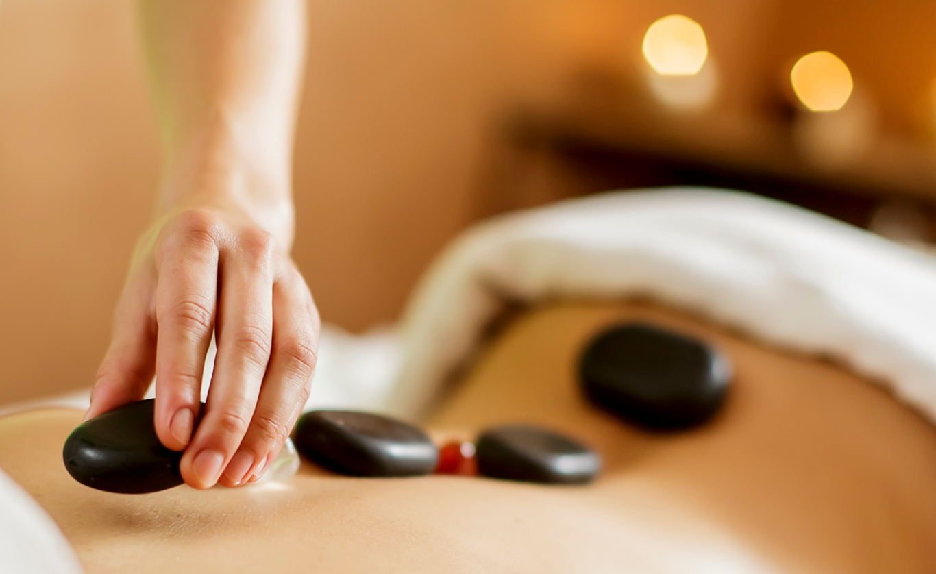 Masaje con Piedras Calientes Mano colocando piedras calientes sobre el abdomen de una persona durante un masaje.